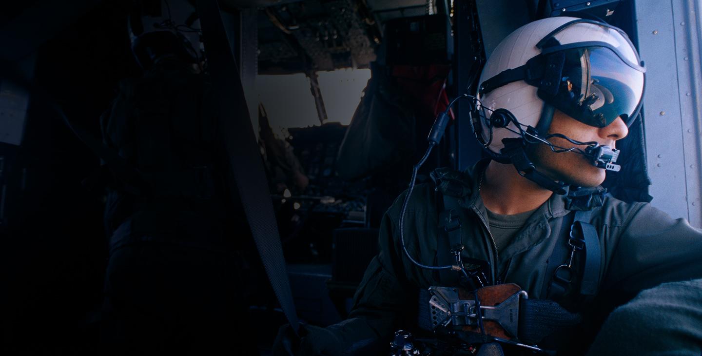一名戴着头盔、眼罩和耳机的男性战士向直升机侧面望去